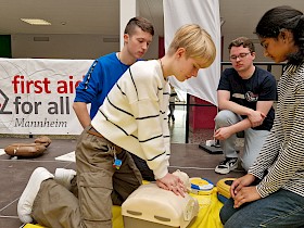 Die Schulsanitäterinnen Lilli Manhart (links) und Umaiza Mohammed Abdul üben die Reanimation mit dem Defribrillator, während Schüler Lukas Wilhelm (links) und Trainer Tobias Haußler (von first aid for all) das Geschehen aufmerksam verfolgen.